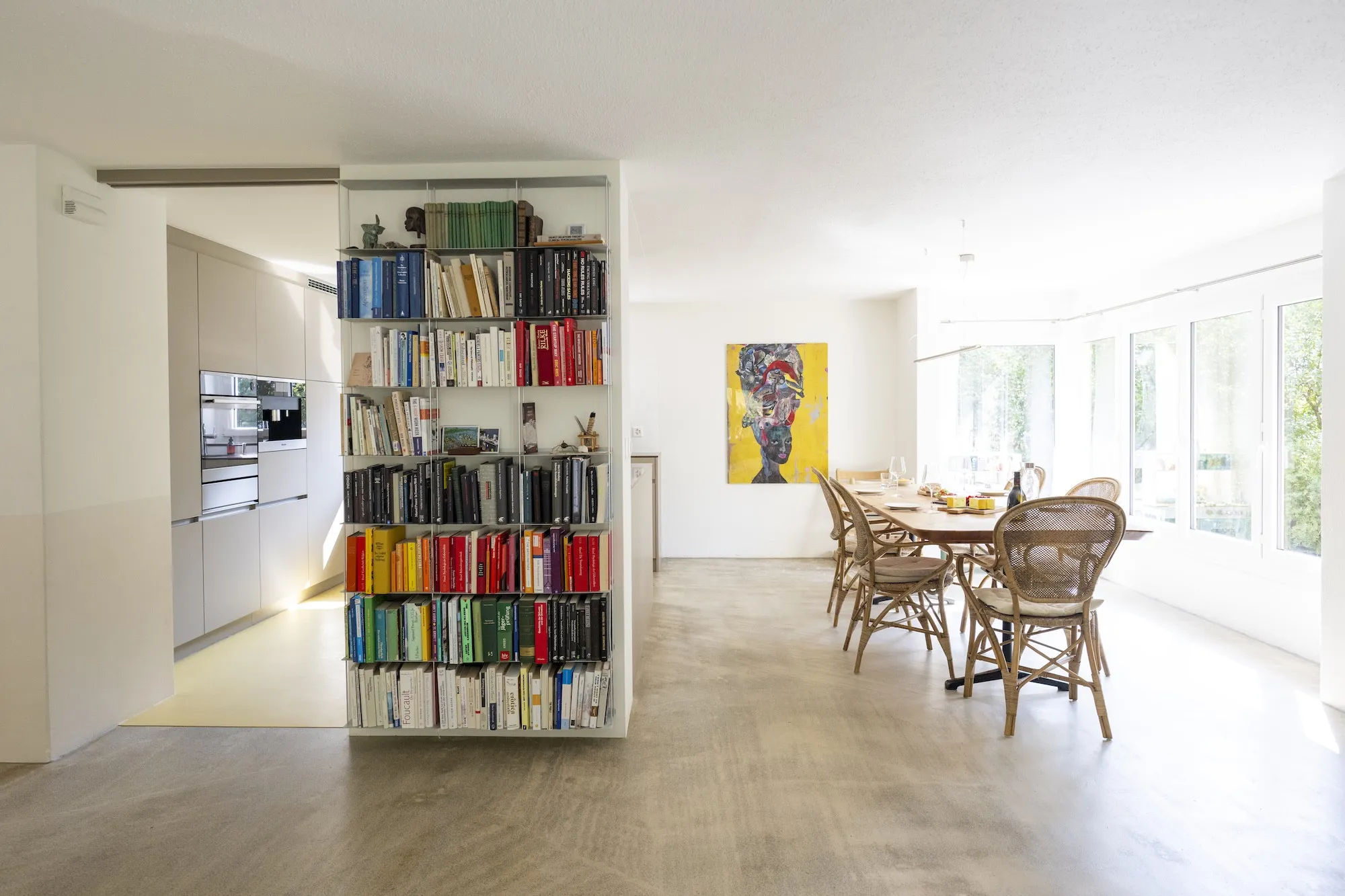 Der grosse Esstisch neben Bücherregal und offener Küche